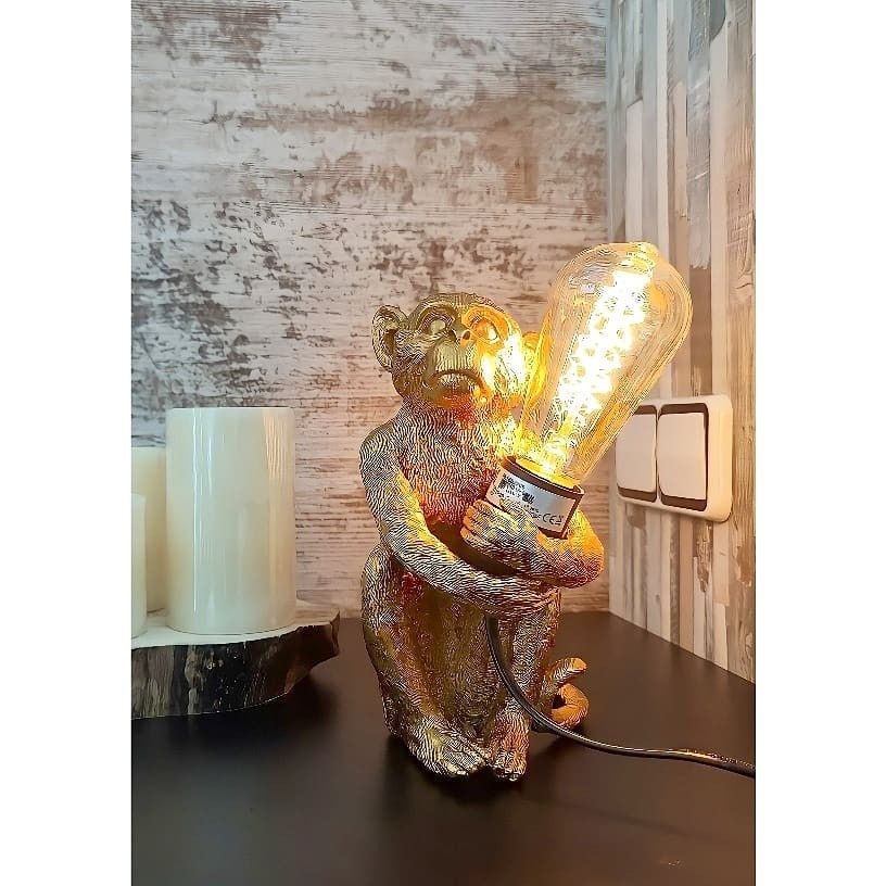 Una lámpara de mesa dorada con forma de mono sostiene una bombilla Edison brillante de estilo vintage