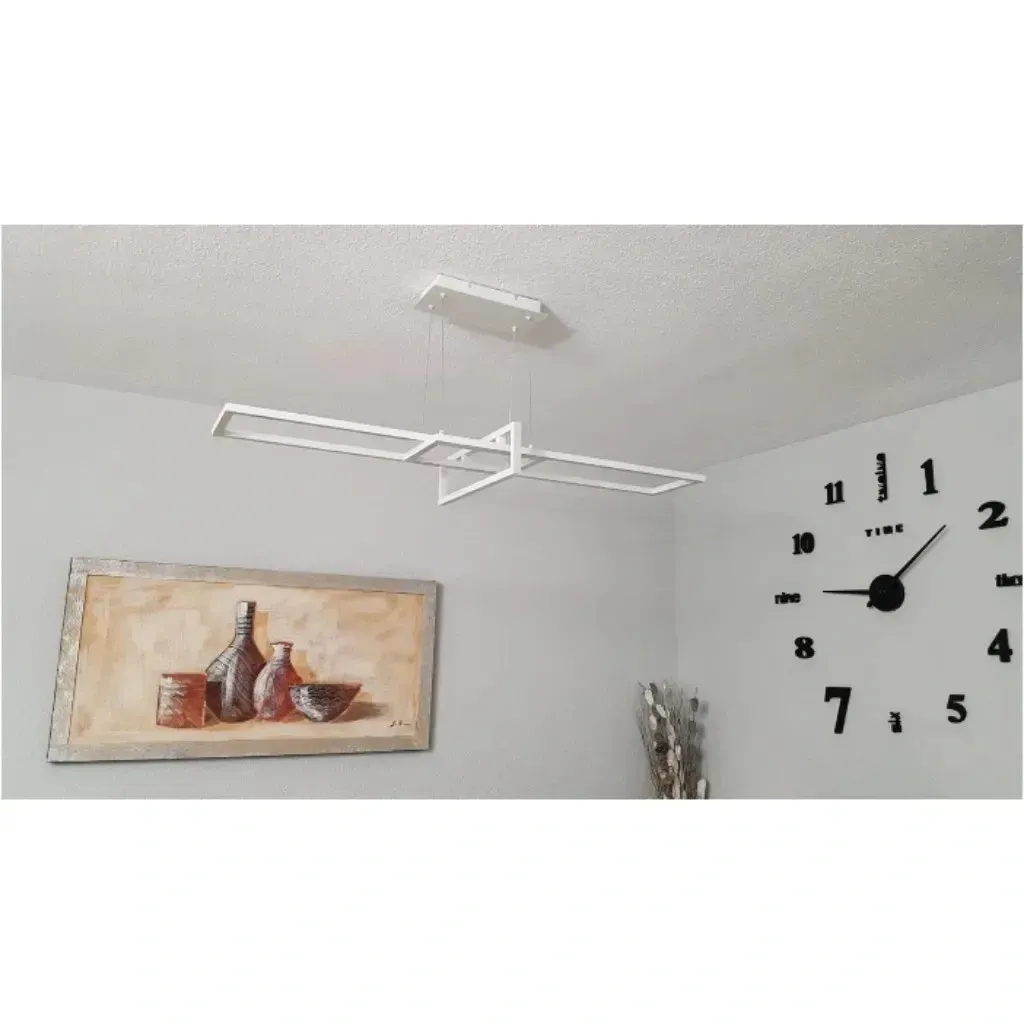 Una moderna lámpara rectangular blanca cuelga del techo cerca de un cuadro de naturaleza muerta enmarcado