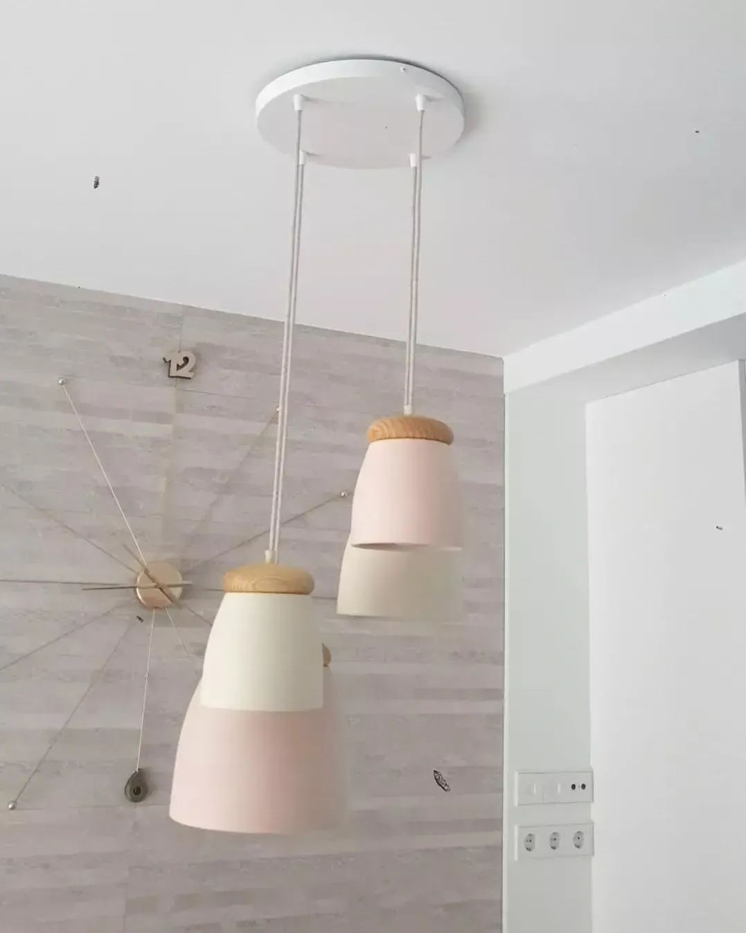 Dos lámparas colgantes con remates de madera clara y pantallas de cerámica en tonos rosa y crema