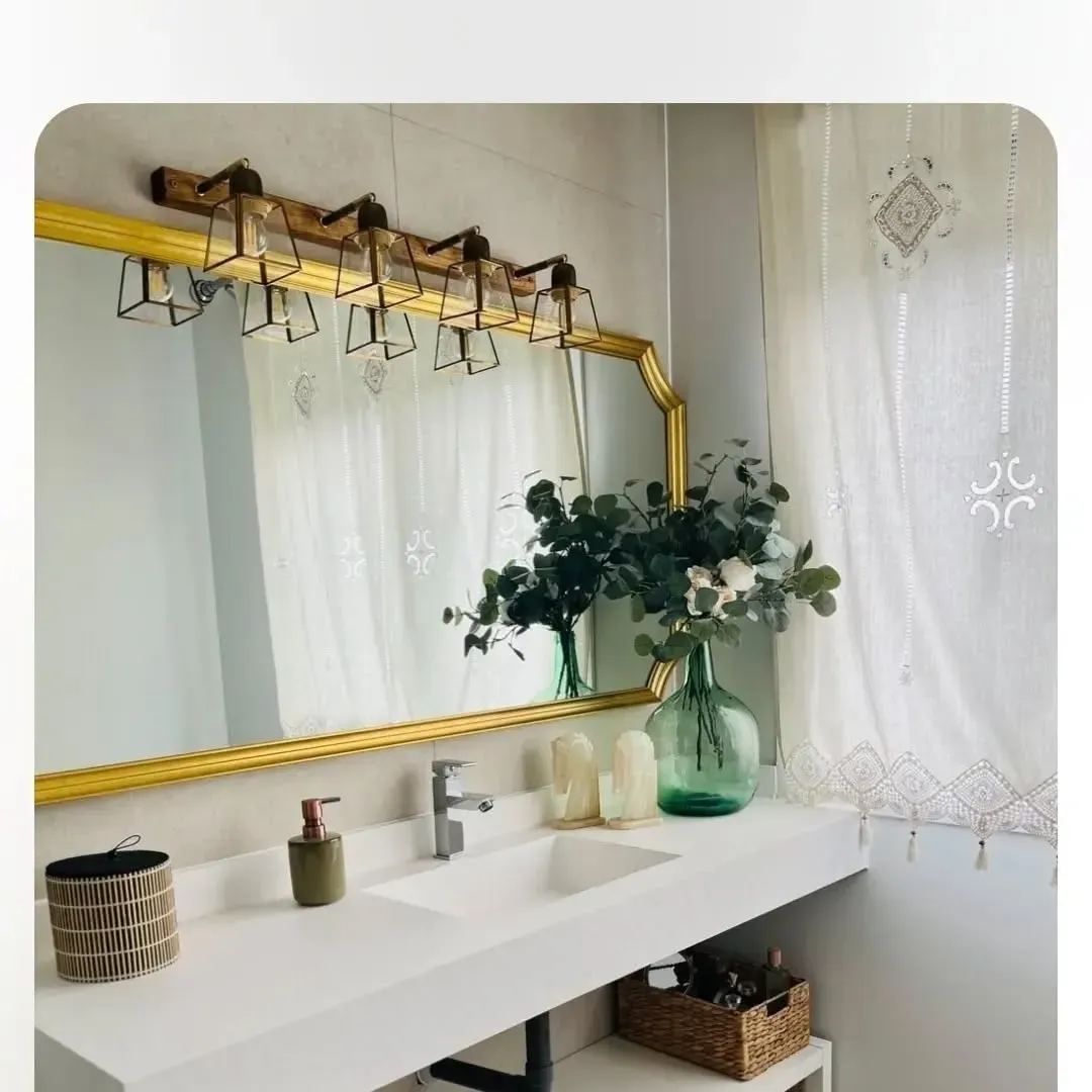 Tocador de baño moderno con encimera blanca, espejo con marco dorado, lámpara de cinco luces