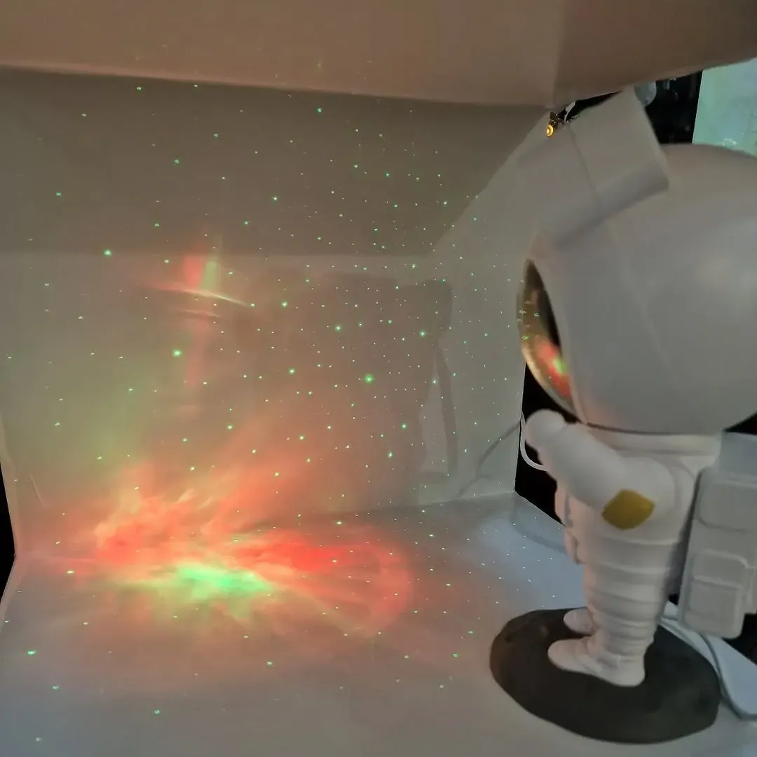 Una pequeña figura de astronauta proyecta luces de nebulosa rojas y verdes en espiral, con pequeños puntos