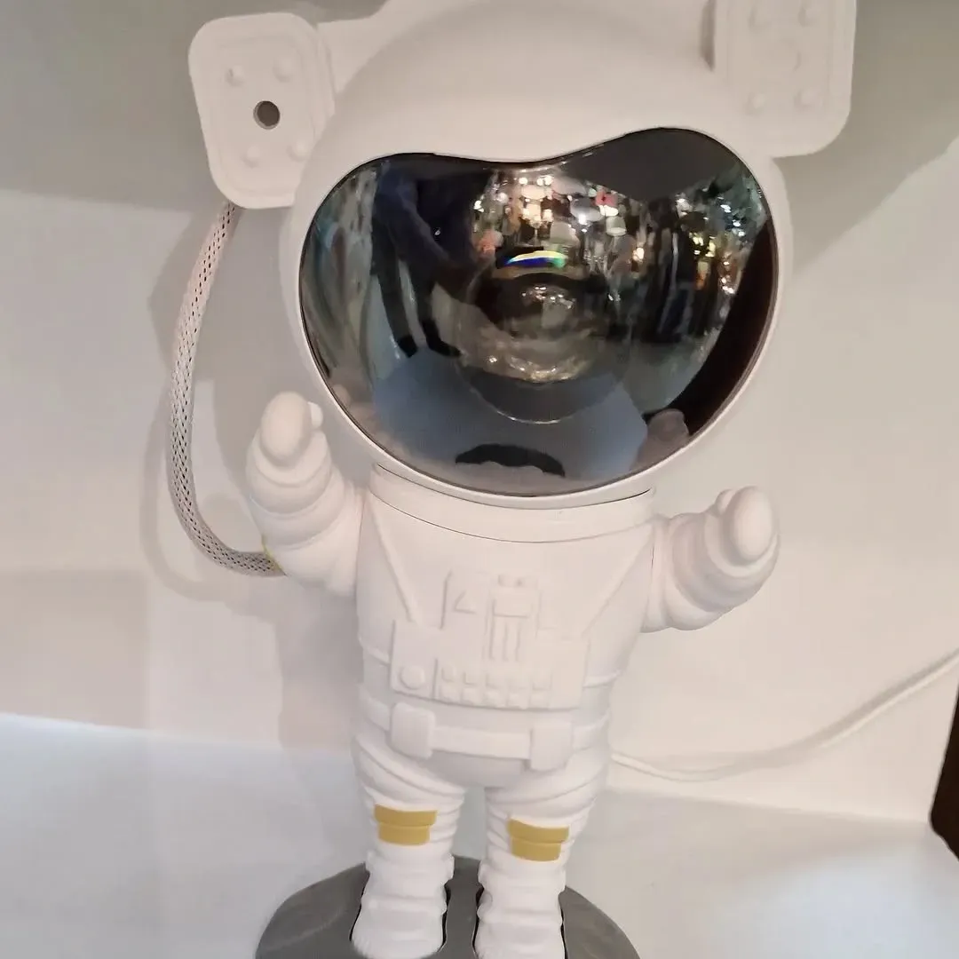 Una lámpara de proyector blanca con forma de astronauta y una placa frontal esférica de cristal oscuro.