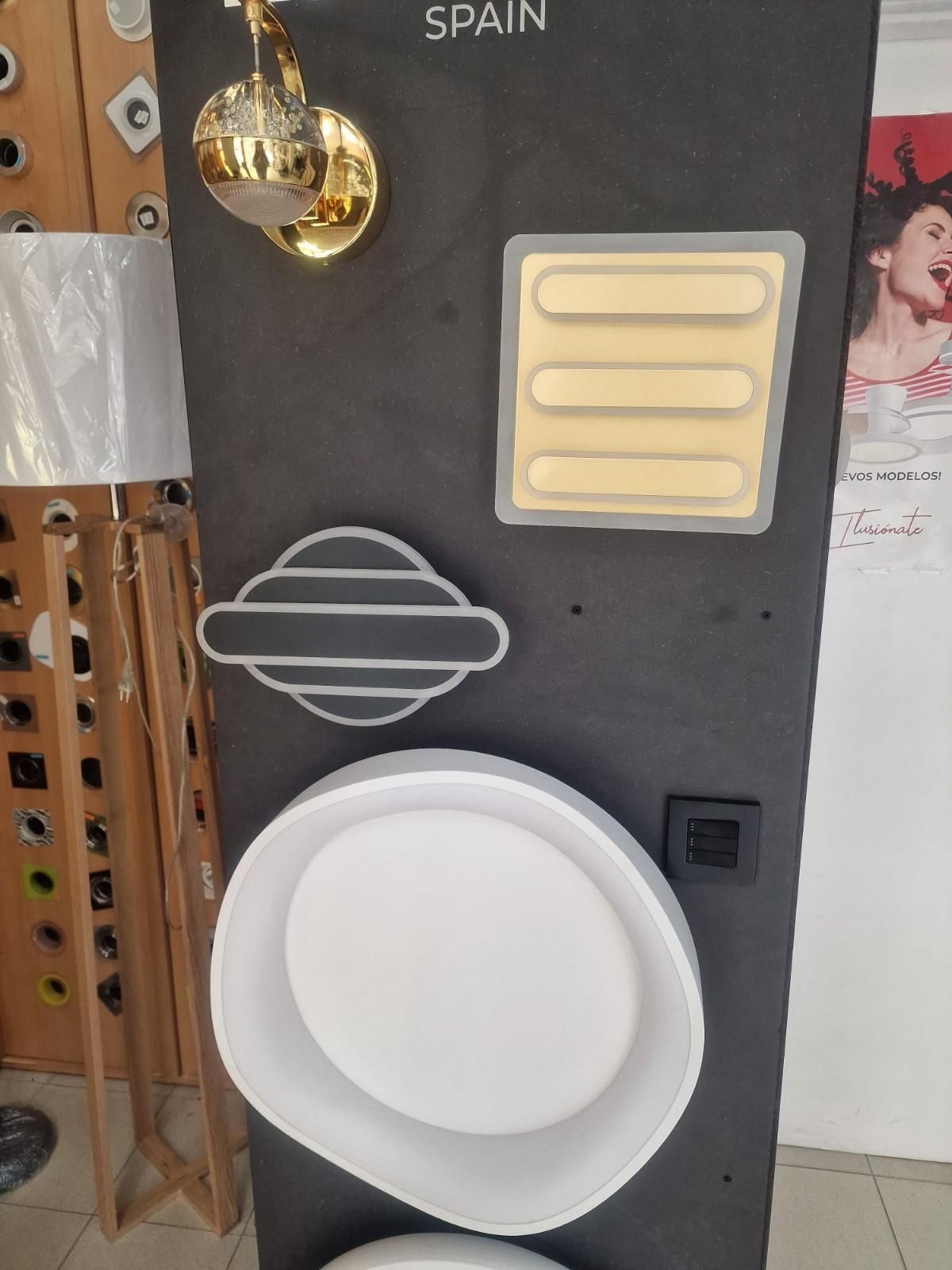 Un panel oscuro que muestra varias luminarias modernas, entre ellas un aplique dorado, un panel cuadrado y lámparas redondas.