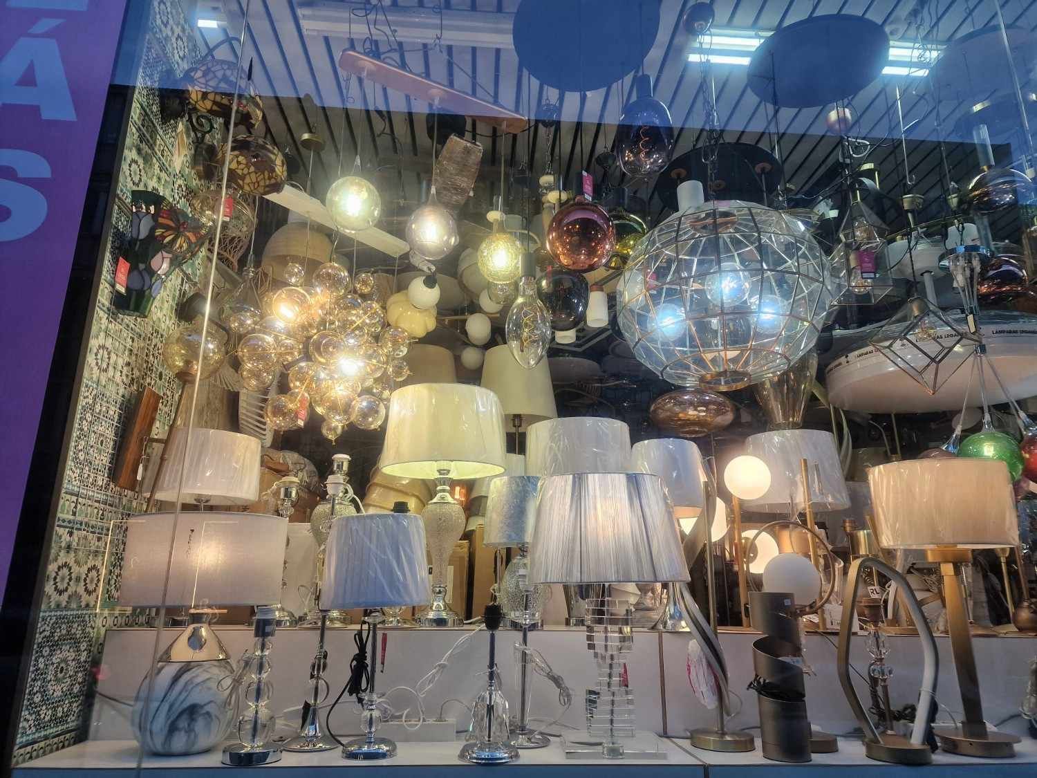Un escaparate con numerosas lámparas de mesa iluminadas y lámparas colgantes de diversas formas y estilos.
