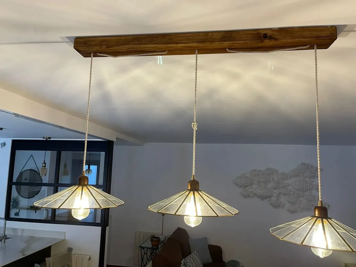 Tres lámparas colgantes con pantallas de cristal geométricas y bombillas Edison suspendidas de una viga de madera.