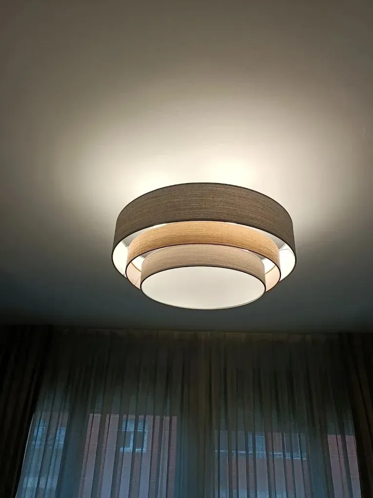 Una lámpara de techo circular de tres niveles, hecha de tela beige, que emite una luz cálida