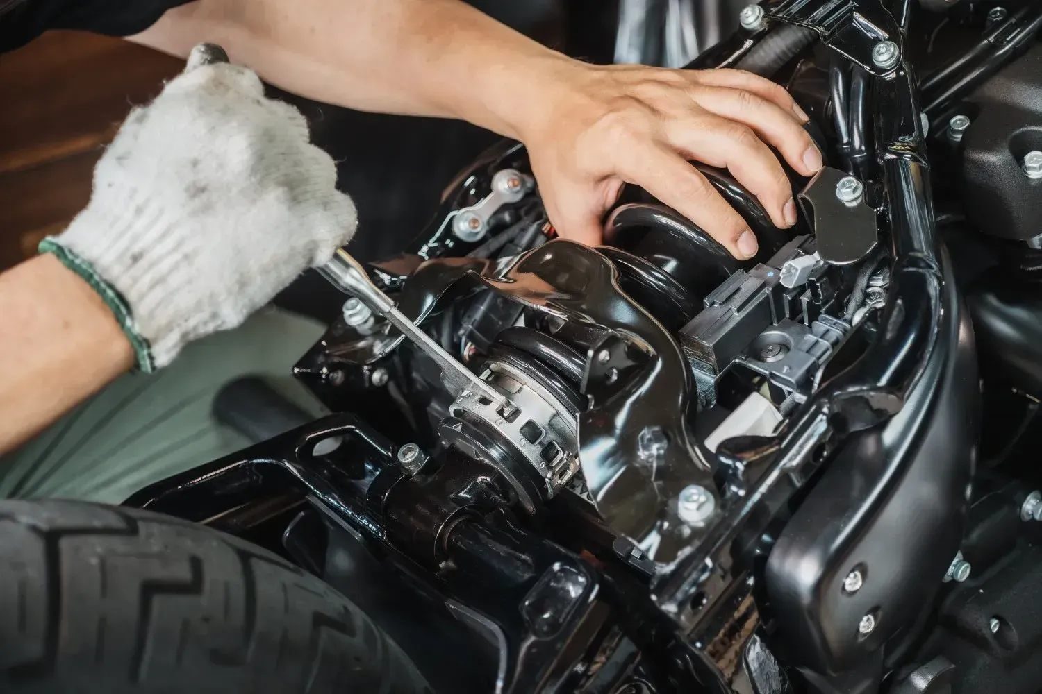 Persona que utiliza una llave inglesa en una motocicleta negra, usando un guante.