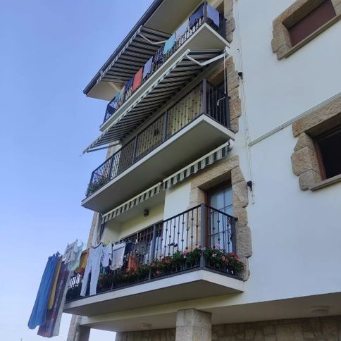 Edificio de apartamentos de varios pisos con balcones, ropa tendida, toldos extendidos y detalles de piedra visibles.