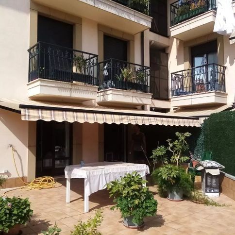 Un patio con toldo color crema, mesa y macetas. Arriba, balcones con barandillas negras.