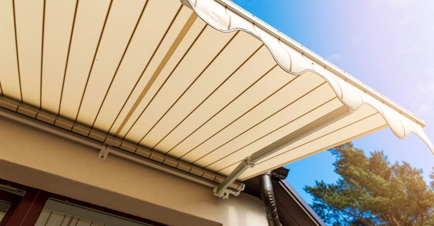 Toldo retráctil beige que se extiende desde una casa, fondo de cielo azul.