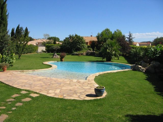 Une piscine en béton se dresse au milieu d'un gazon verdoyant.