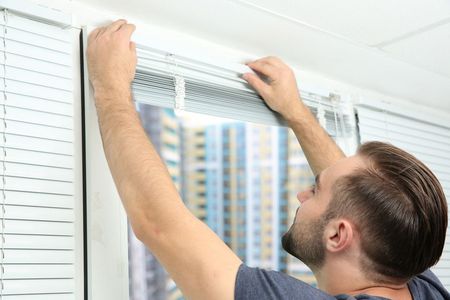 TRIJAG GMBH – ein Monteur installiert eine Jalousie an einem Fenster