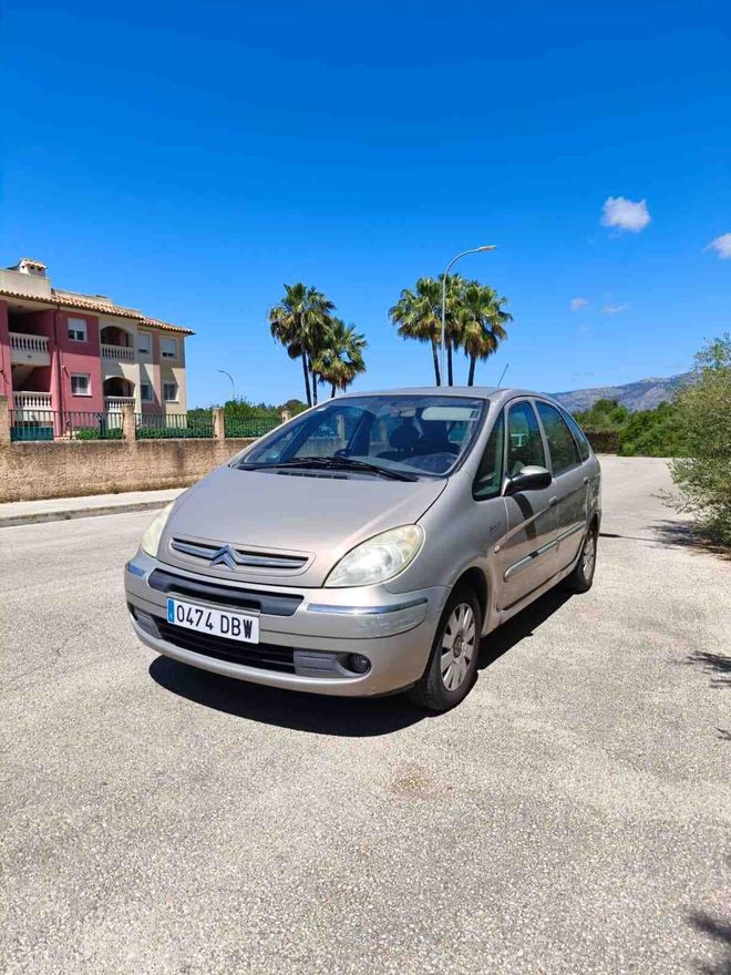 Coche compacto plateado aparcado en una soleada cuneta cerca de palmeras y edificios de apartamentos.