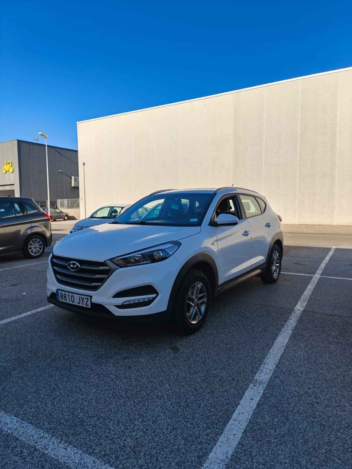 SUV blanco estacionado en un estacionamiento rayado junto a un edificio beige bajo un cielo azul despejado.