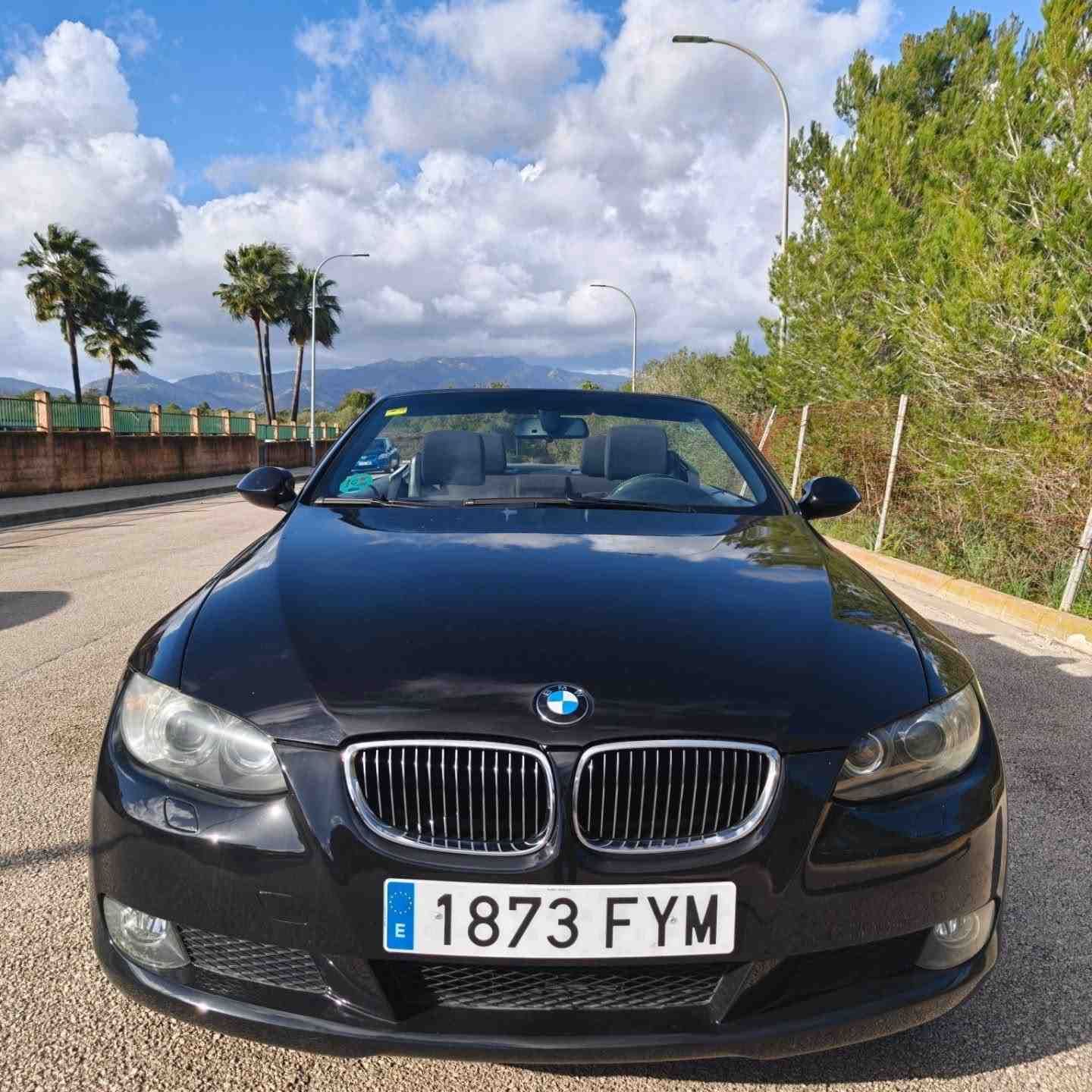 Un BMW descapotable negro aparcado en una carretera soleada con montañas y palmeras al fondo.