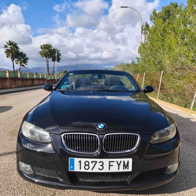 Un BMW descapotable negro aparcado en una carretera soleada con montañas y palmeras al fondo.