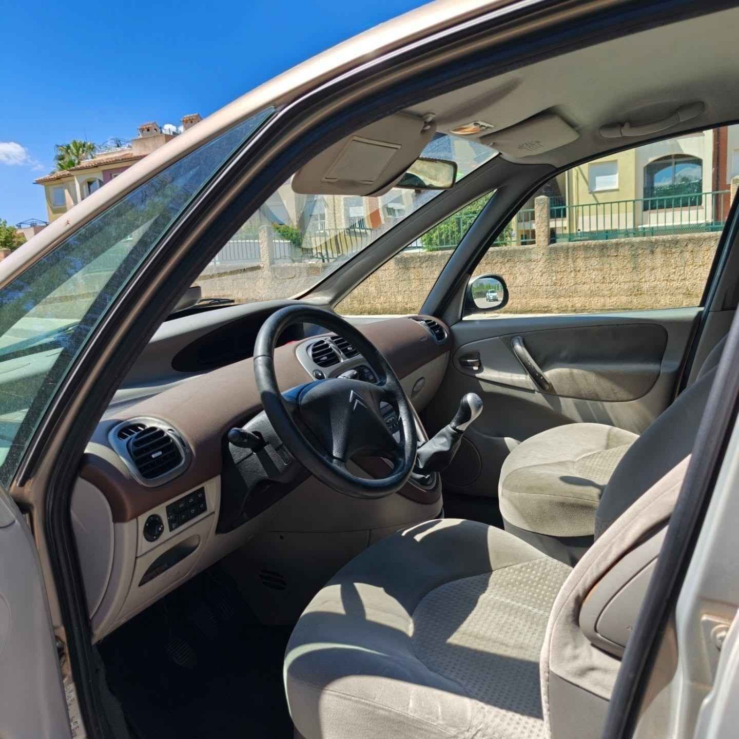 Interior del coche con asientos y volante de color beige, y la puerta del conductor abierta, bañado por la luz del sol.