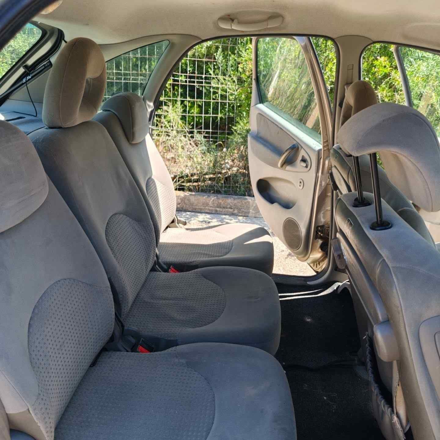 Interior del coche con asientos de tela gris y la puerta trasera abierta, que deja ver la vegetación exterior.