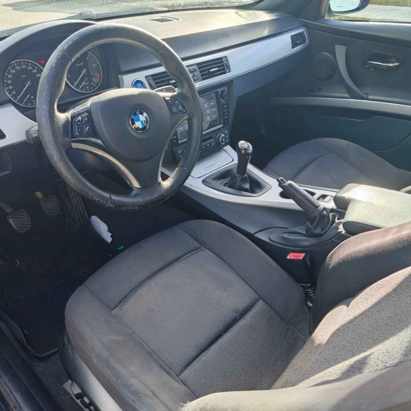 Interior de un automóvil BMW con asientos, volante y consola central negros, visto desde el lado del conductor.