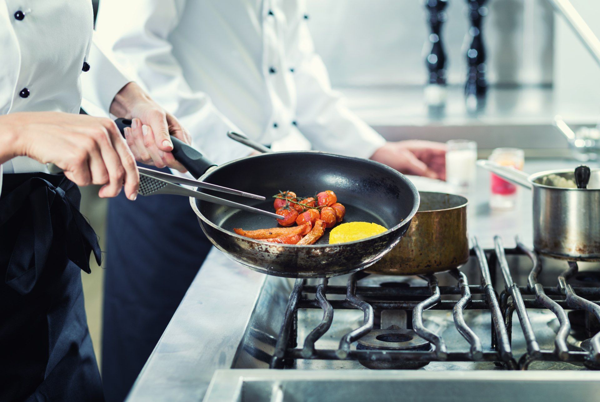 Person hält Pfanne über Gasherd in Großküche