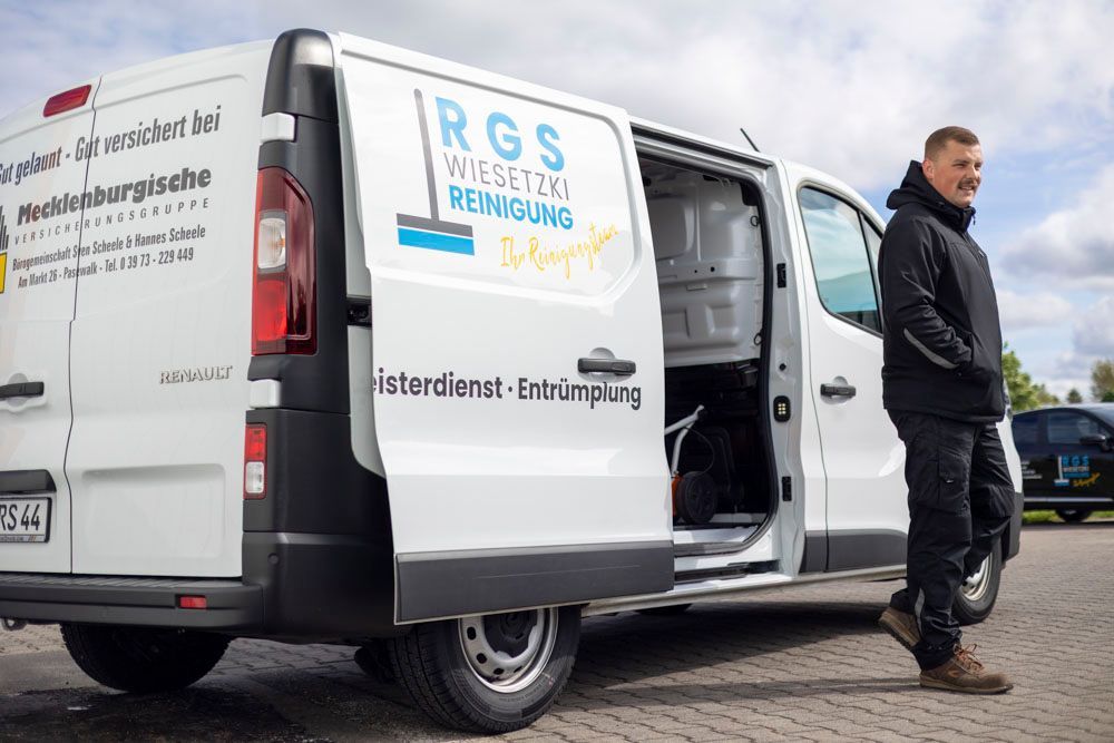 Weißer Lieferwagen mit offener Hecktür und Logo, geparkt am Bürgersteig, ein Mann steht daneben.