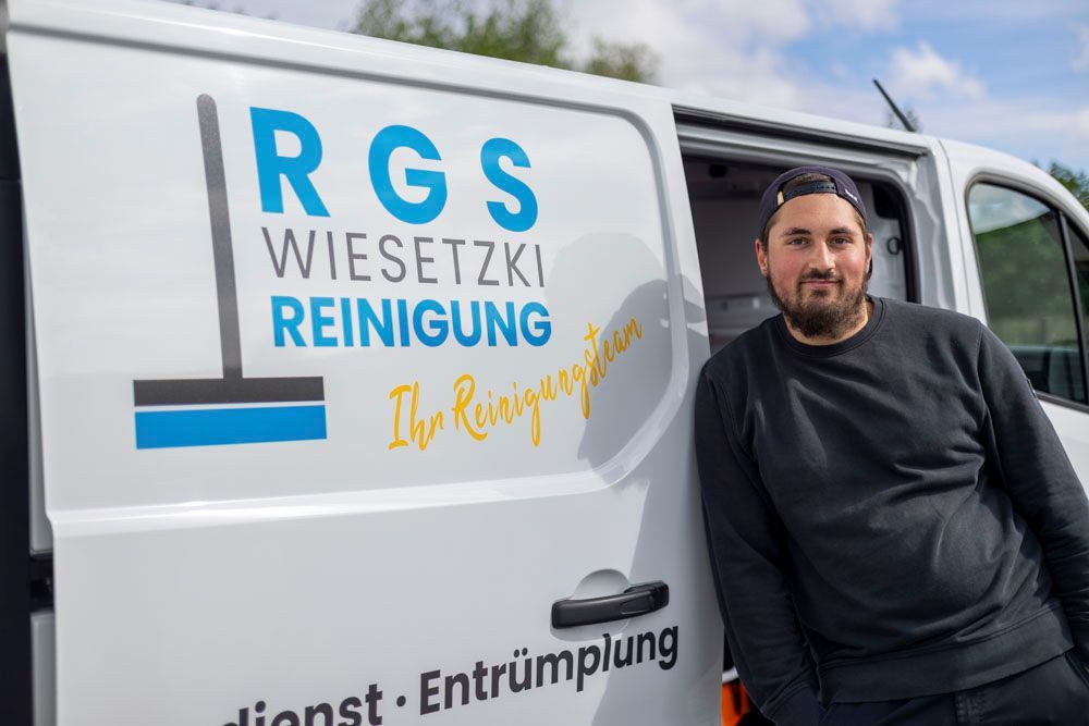 Ein Mann steht neben einem weißen Lieferwagen mit dem Logo und dem Text „RGS Wiesetki Reinigung“.
