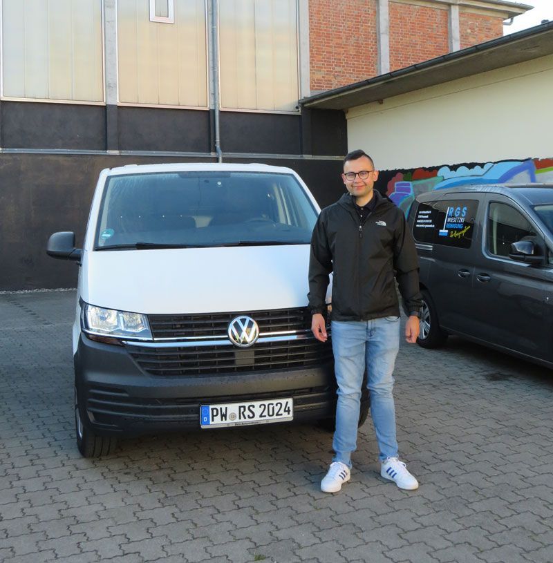 Ein Mann steht vor einem Volkswagen-Transporter mit einem Nummernschild, auf dem „PH RS 2024“ steht