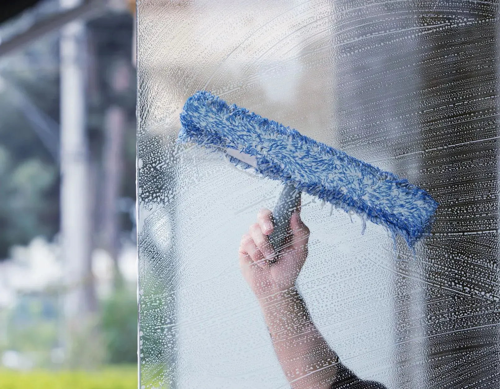 Fensterreinigung per Hand mit blauem Schwamm.