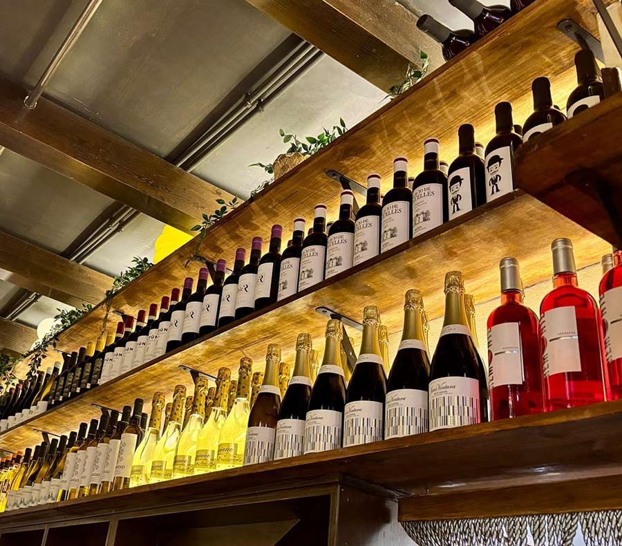 Estanterías repletas de botellas de vino y champán de diversos tipos, expuestas en un bar o restaurante con iluminación cálida.