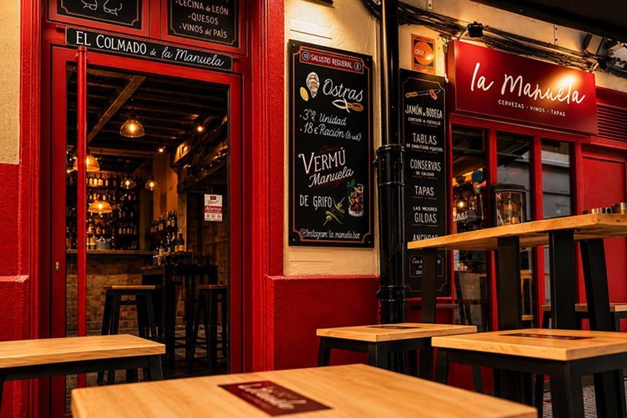 Fachada de cafetería pintada de rojo con pizarras para el menú y mesas vacías al anochecer.
