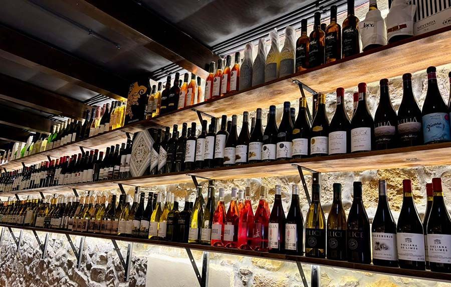 Filas de botellas de vino expuestas en estantes iluminados en un bar o vinoteca.