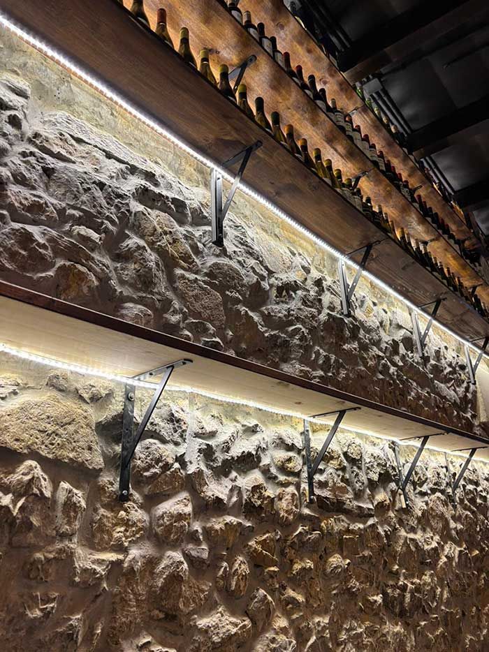 Muro de piedra con vigas metálicas y una hilera de luces bajo un techo oscuro.