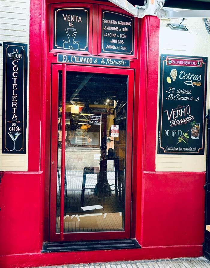 Fachada roja con puerta de cristal, menús en pizarra negra y molduras blancas.