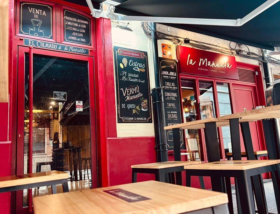 Entrada roja de la cafetería con pizarra para el menú, mesas de madera y luces de guirnalda cálidas.