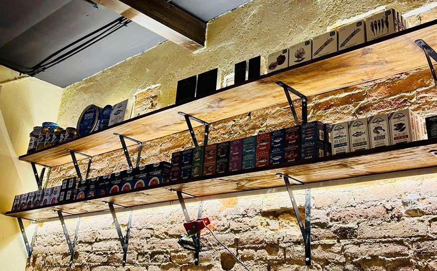 Estanterías con cajas de productos y utensilios de cocina contra una pared de piedra rústica en el interior de una tienda.