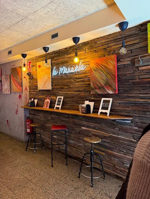 Interior de un restaurante con pared de madera, mostrador, taburetes, arte y lámparas colgantes.