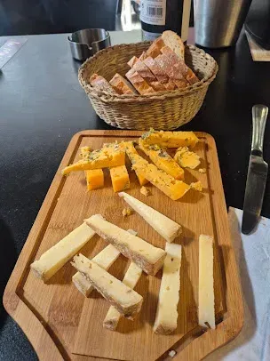 Tabla de quesos con pan de molde en una cesta. Incluye dos tipos de queso y un cuchillo sobre una tabla de madera.