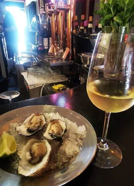 Ostras en hielo con una rodaja de lima y una copa de vino blanco en un bar.