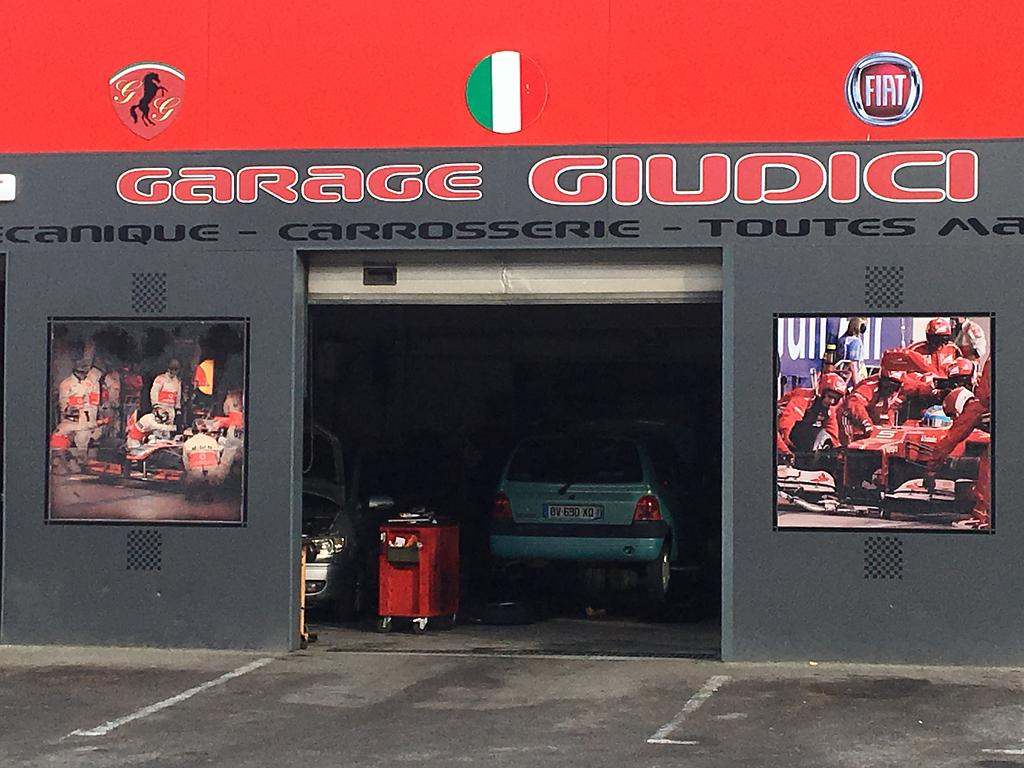 Façade du garage Giudici avec une baie ouverte et deux affiches murales