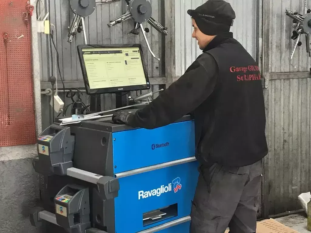 Technicien utilisant un ordinateur portable devant un appareil de diagnostic bleu dans un atelier