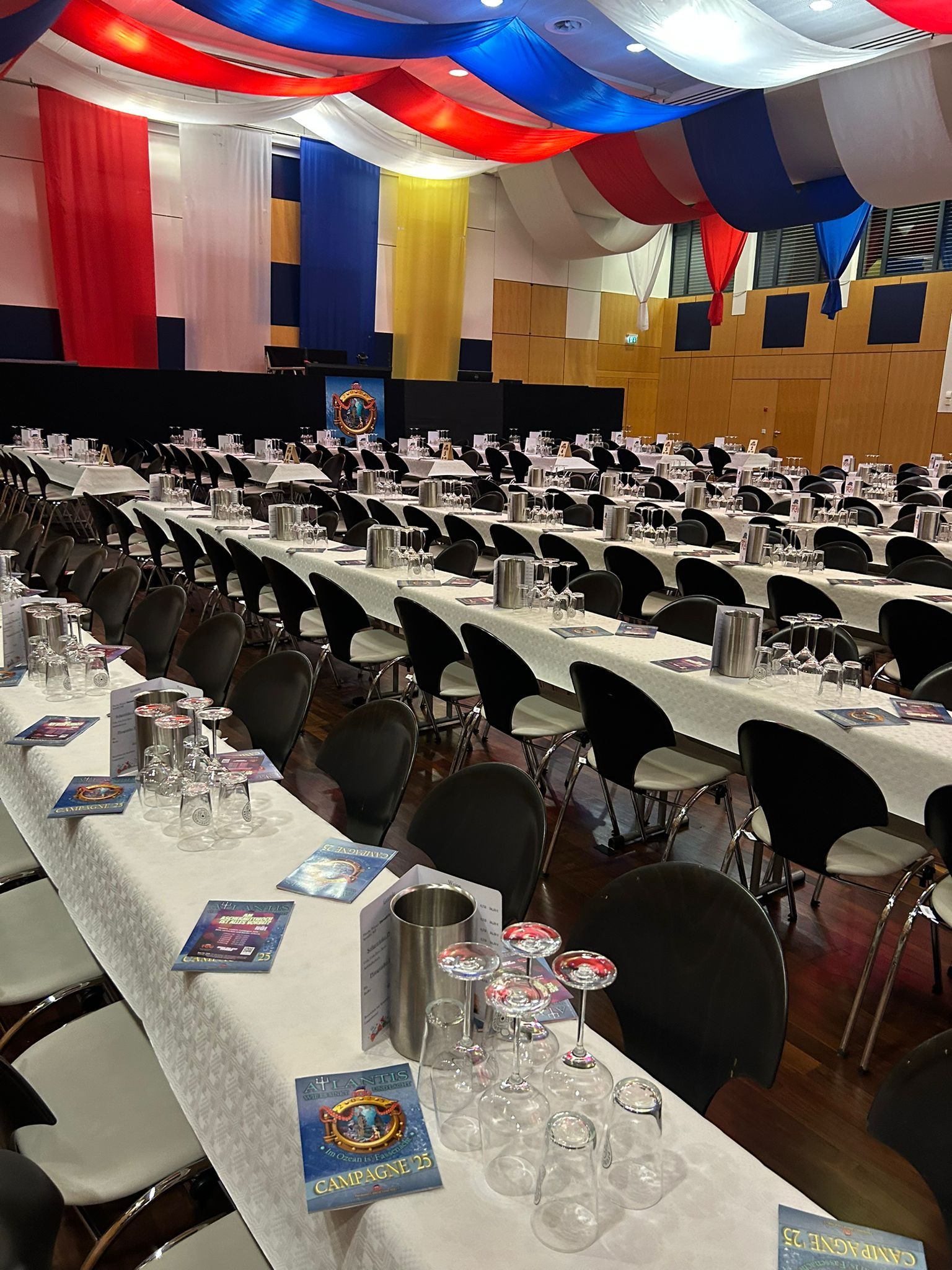 Festsaal mit langen weißen Tischen, schwarzen Stühlen und rot-blau-weiß drapierten Deckendekorationen