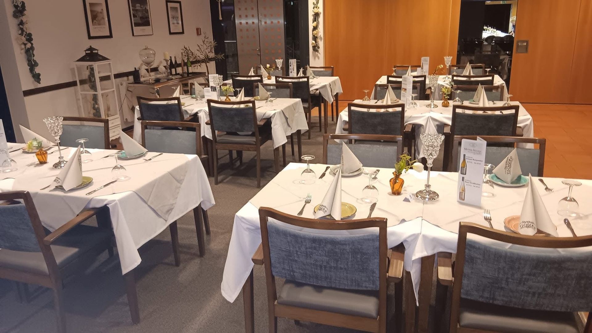 Leerer Speisesaal des Restaurants mit gedeckten Tischen, weißen Tischdecken, Stühlen und Wandbildern