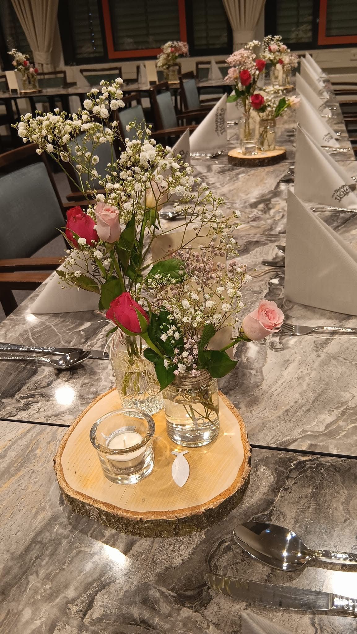 Ein festlich gedeckter Tisch mit weißen Servietten, Blumengestecken und Kerzenlicht in einem schwach beleuchteten Raum