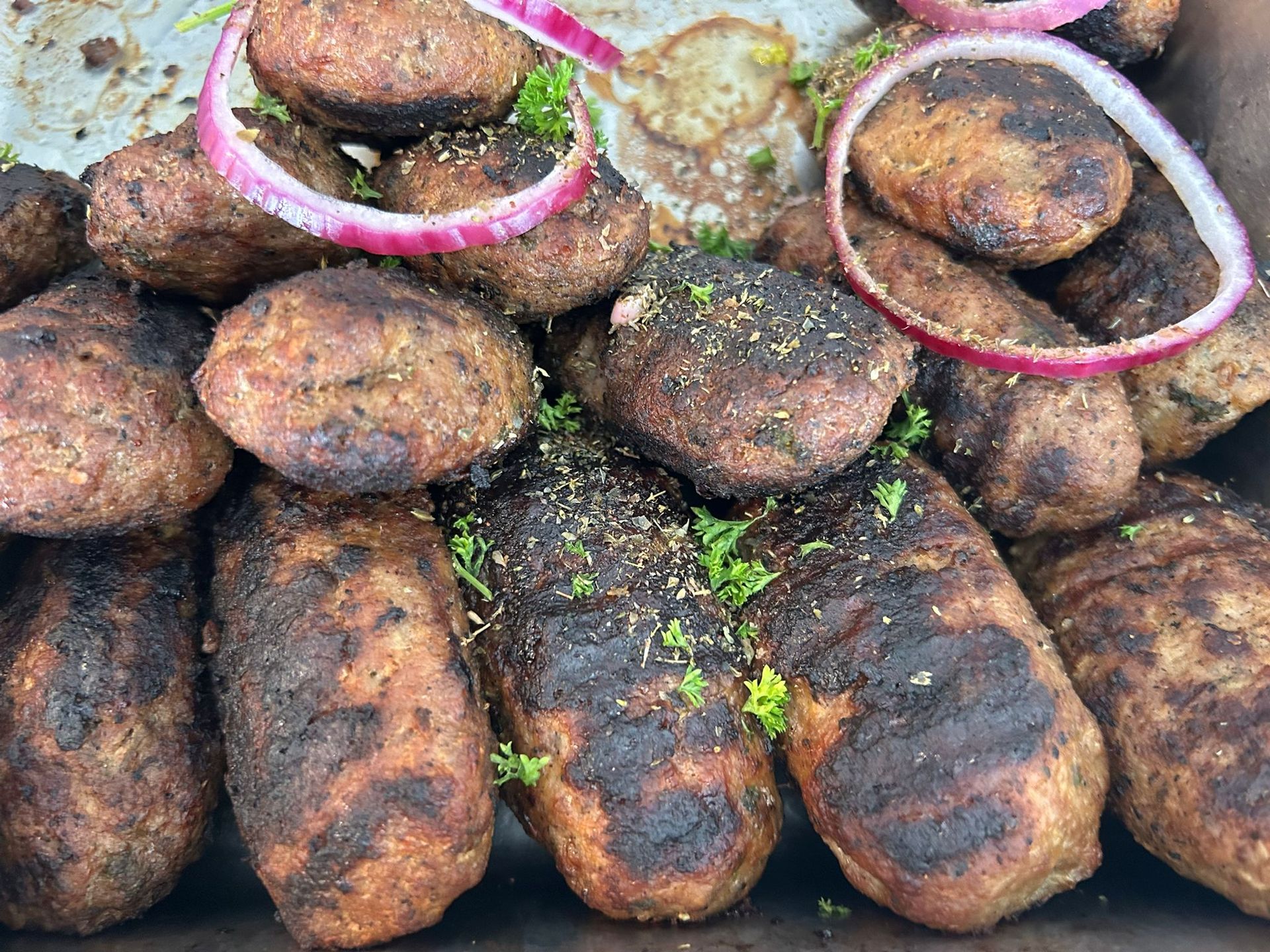 Gegrillte Frikadellen, gestapelt mit Zwiebelringen und Kräutern auf einem Tablett