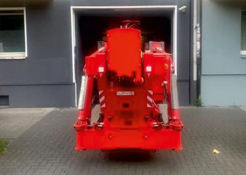 Rückansicht eines roten Feuerwehrautos, das vor einem grauen Gebäude mit einer garagenähnlichen Öffnung geparkt ist.