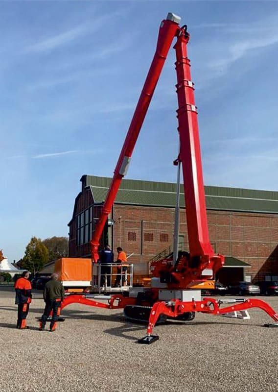 Roter Spinnenlift mit Arbeitern an einem Gebäude an einem sonnigen Tag.