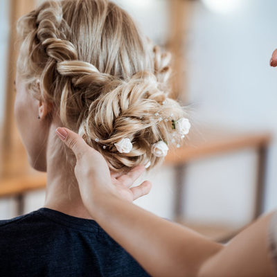 Eine blonde Flechtfrisur wird in einem hellen, salonähnlichen Ambiente von Hand gestylt.