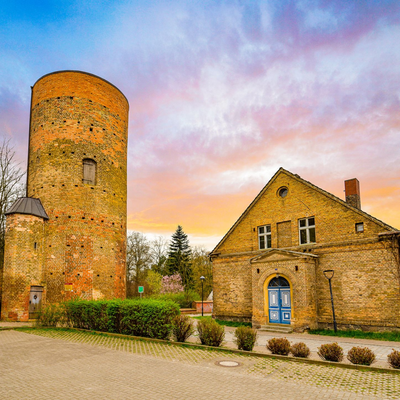 Historischer Steinturm und Gebäude im Sonnenuntergang, vor farbenprächtigem Himmel und Kopfsteinpflasterhof.