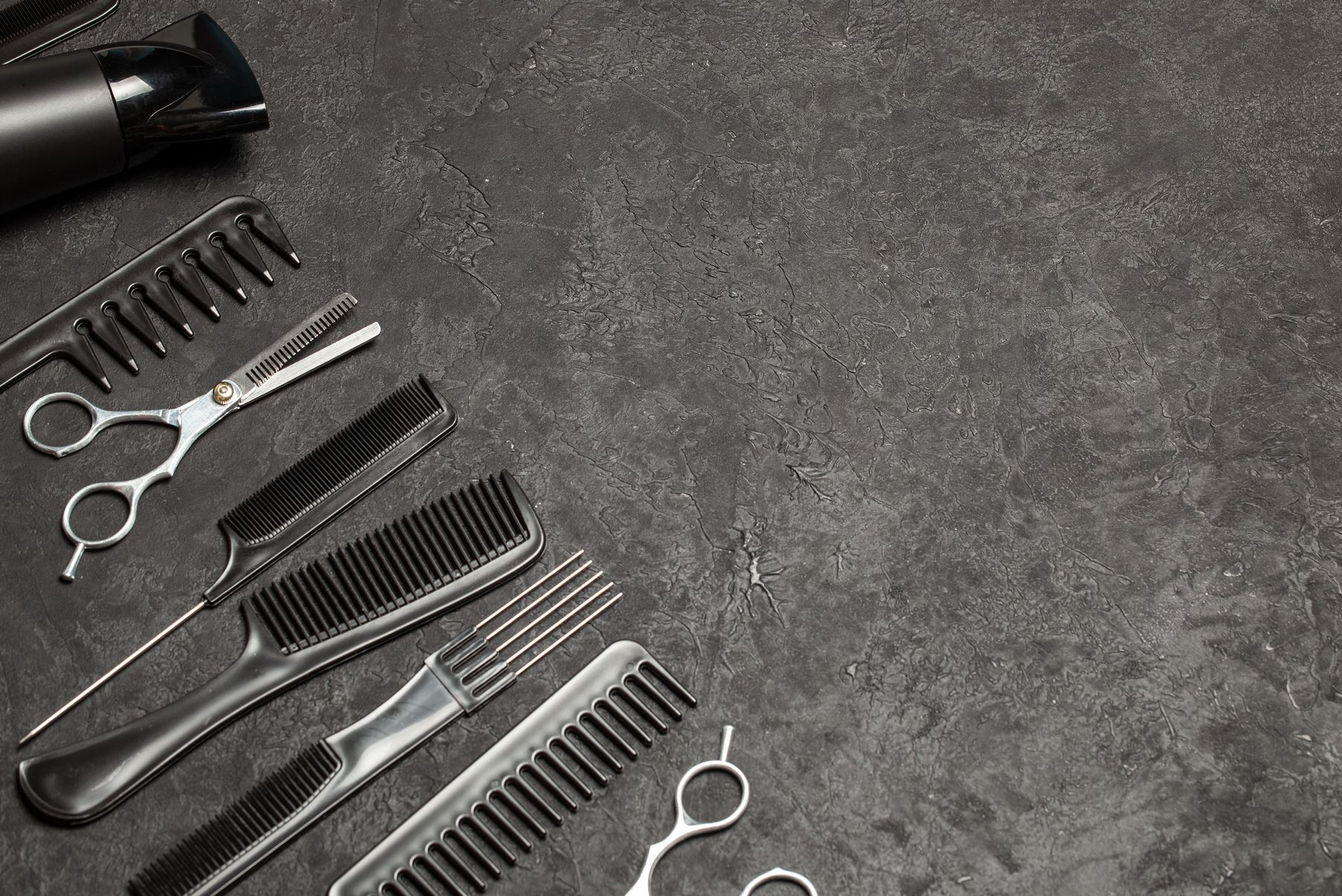 Verschiedene schwarze Friseursalon-Werkzeuge und Kämme sind auf einer dunklen, strukturierten Oberfläche angeordnet.