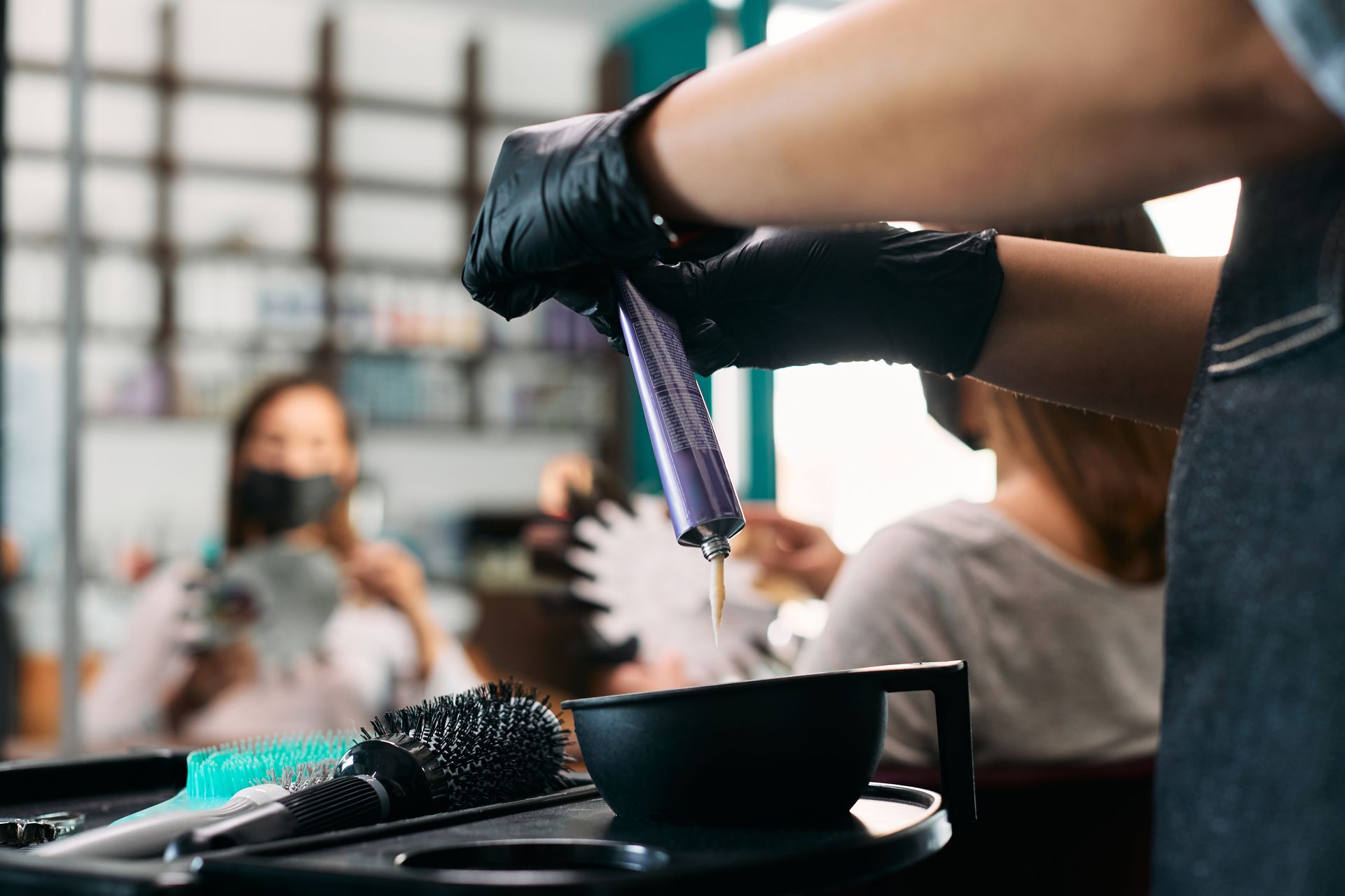 Eine Friseurin färbt in einem Salon die Haare lila; Pinsel und Schale stehen auf der Ablage.